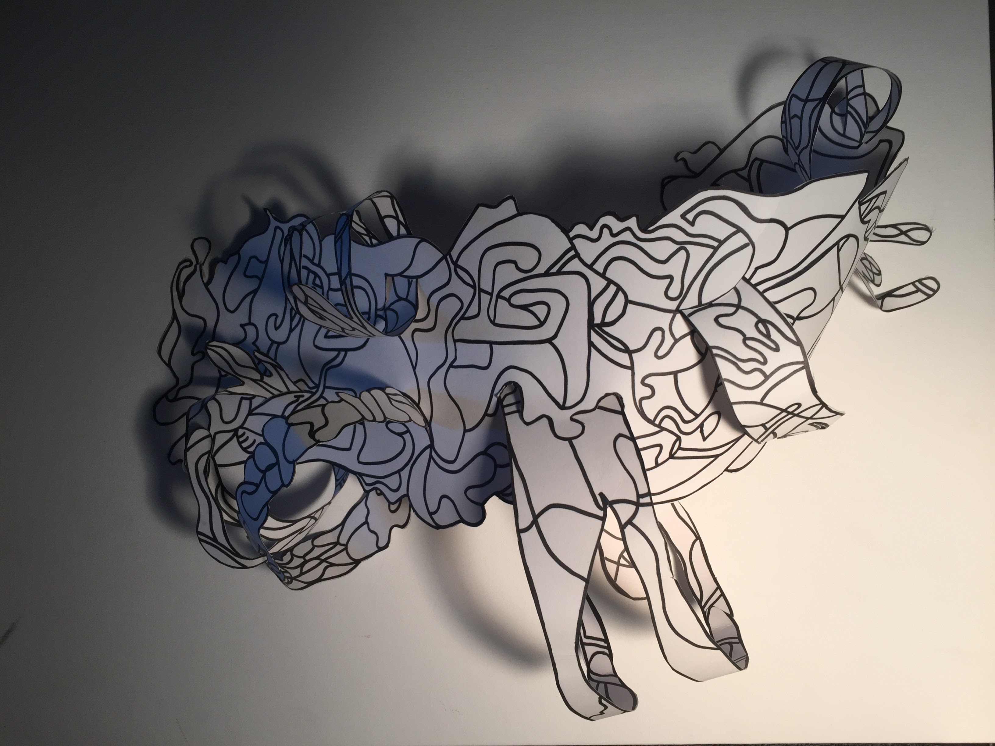 A close-up of one of Angie’s paper sculptures: layered, line-drawn shapes lit from the side with dramatic shadows.